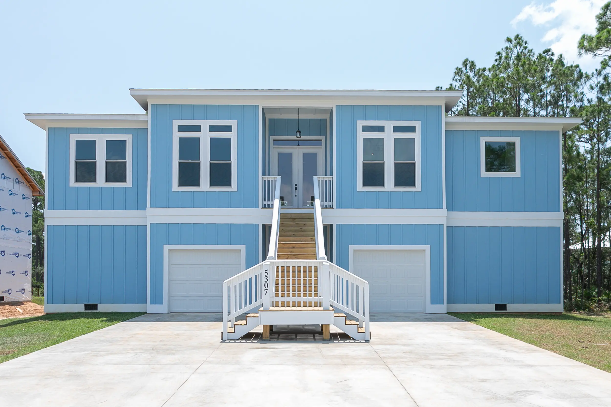 Blue elevated house with white stairs and garage doors below.
