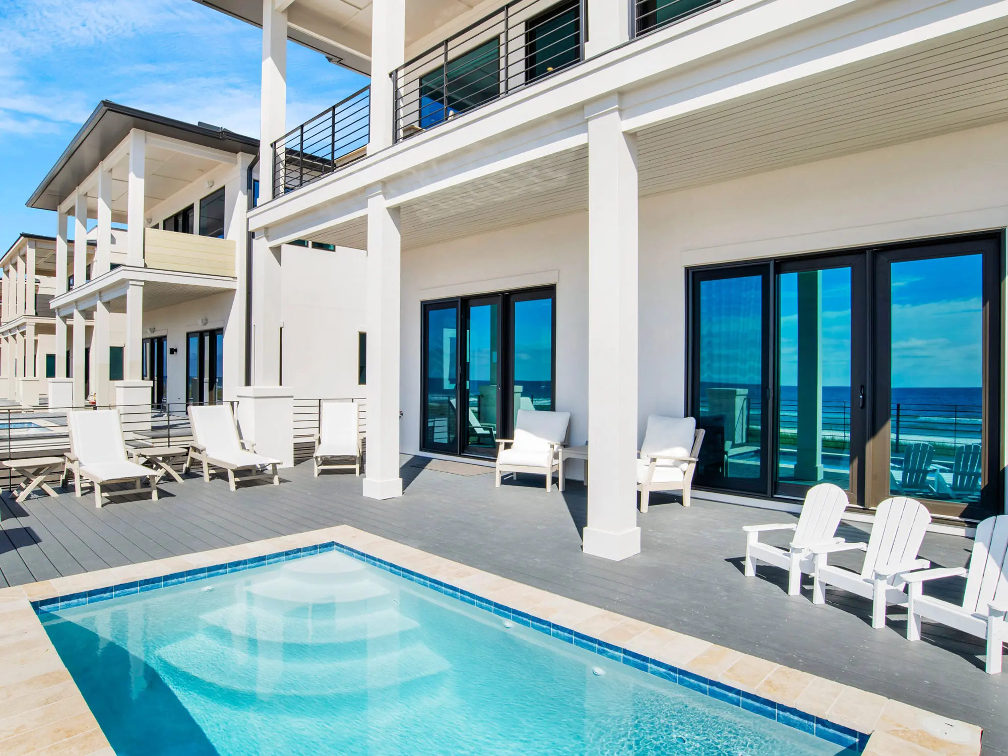 Modern poolside patio with white furniture and ocean view.