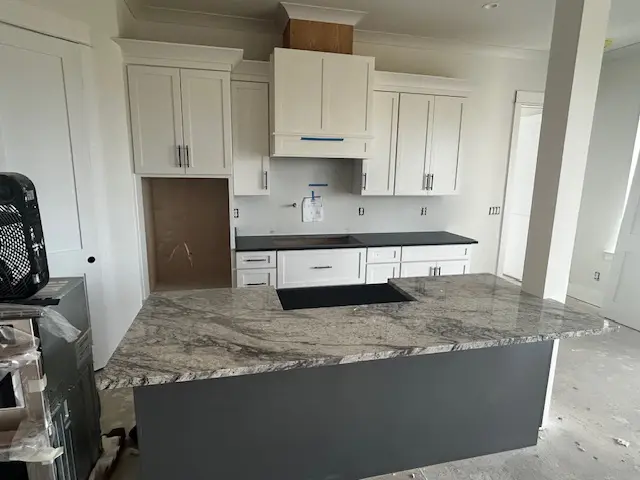 Modern kitchen with marble countertop and white cabinets.