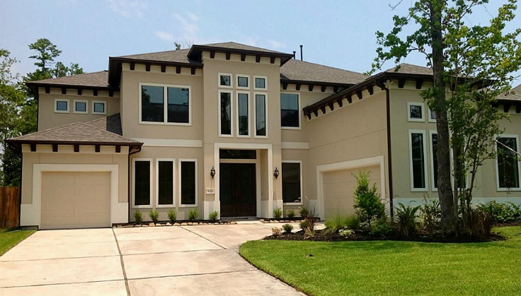 Modern two-story beige house with large windows and a manicured lawn.